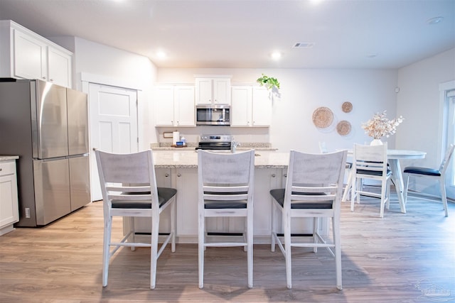 kitchen with light stone countertops, light wood-style flooring, white cabinetry, visible vents, and appliances with stainless steel finishes