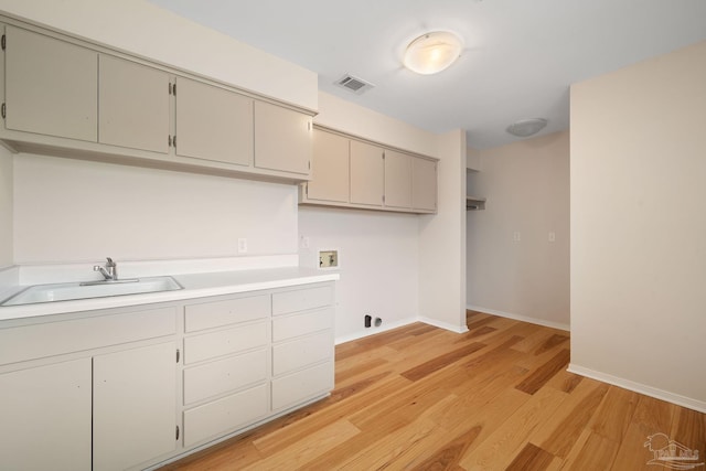 laundry room featuring sink, hookup for a washing machine, light hardwood / wood-style flooring, and cabinets