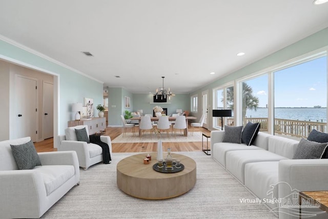 living room featuring an inviting chandelier, light hardwood / wood-style flooring, ornamental molding, and a water view