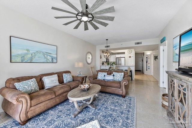 living room featuring ceiling fan with notable chandelier, a textured ceiling, and light tile patterned floors