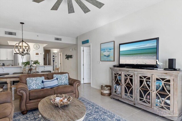 tiled living room with ceiling fan with notable chandelier and a textured ceiling