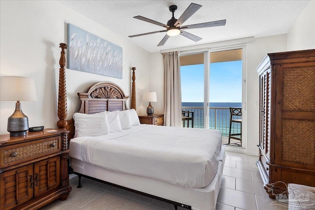 tiled bedroom featuring a water view, a textured ceiling, access to exterior, and ceiling fan