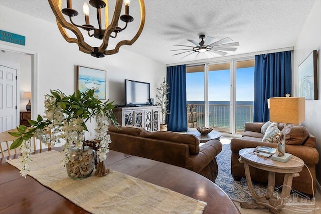 living room featuring ceiling fan with notable chandelier, wood-type flooring, expansive windows, and a textured ceiling