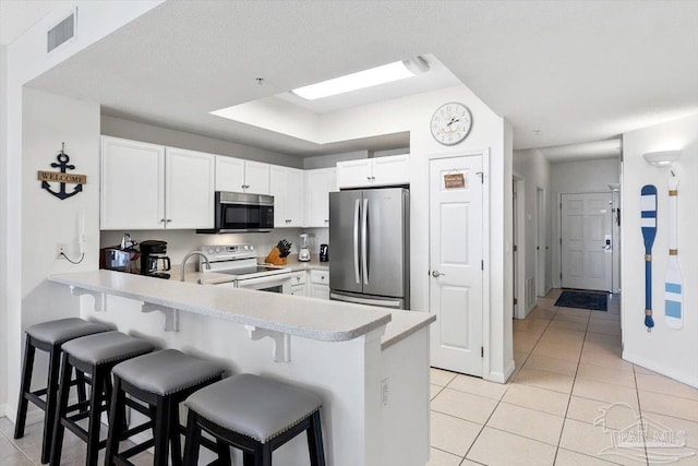 kitchen featuring white cabinetry, stainless steel appliances, a kitchen breakfast bar, and light tile patterned flooring