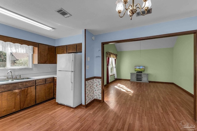 kitchen with light hardwood / wood-style flooring, hanging light fixtures, white fridge, sink, and an inviting chandelier