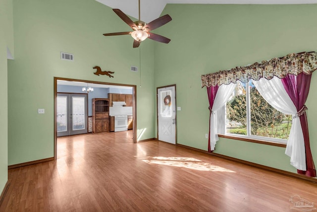 unfurnished living room featuring ceiling fan with notable chandelier, high vaulted ceiling, french doors, and wood-type flooring