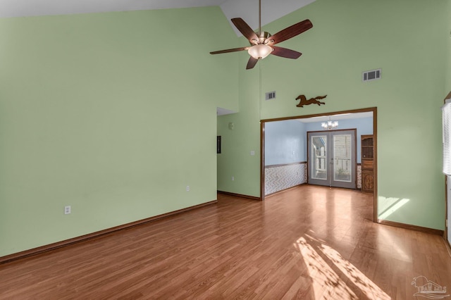 unfurnished living room with french doors, ceiling fan with notable chandelier, high vaulted ceiling, and light hardwood / wood-style flooring