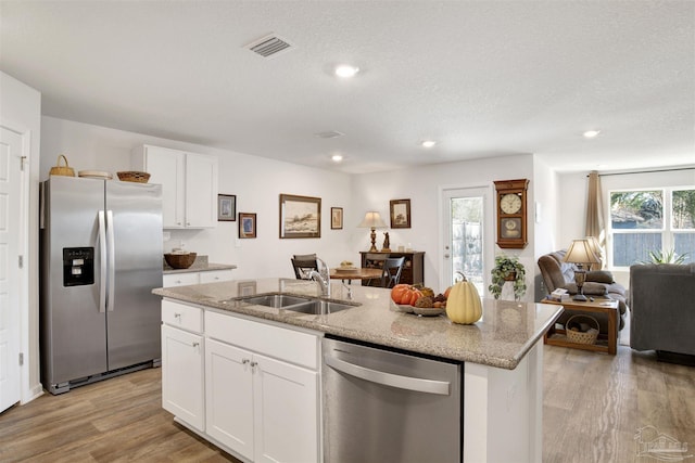 kitchen with appliances with stainless steel finishes, a kitchen island with sink, white cabinets, light stone counters, and sink