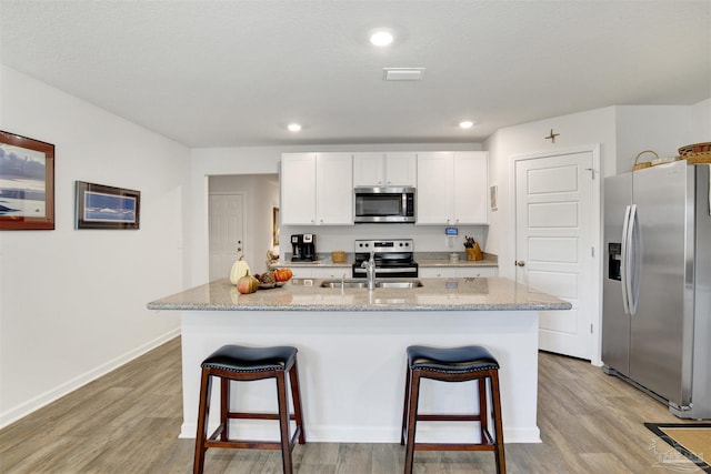 kitchen with light wood-type flooring, white cabinetry, stainless steel appliances, and a center island with sink