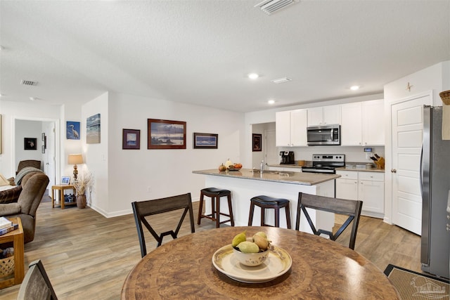 kitchen featuring light wood-type flooring, a kitchen breakfast bar, stainless steel appliances, a textured ceiling, and white cabinets