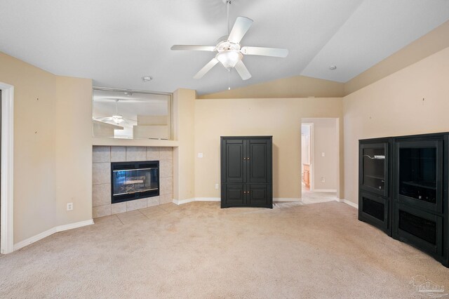 unfurnished living room with a tiled fireplace, vaulted ceiling, light carpet, and ceiling fan