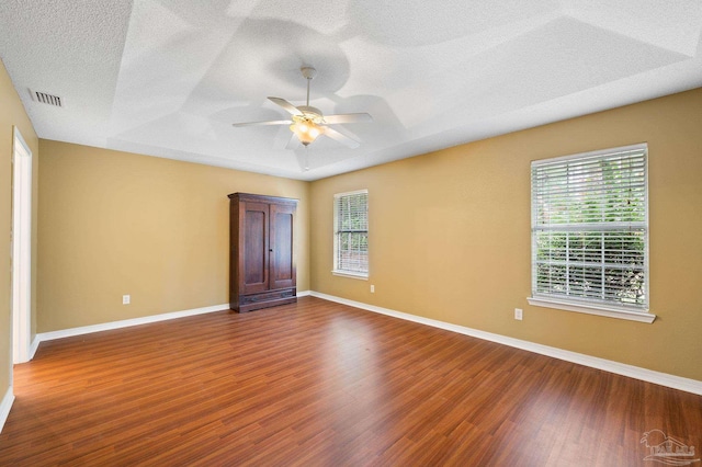 empty room with a wealth of natural light, a raised ceiling, and wood finished floors