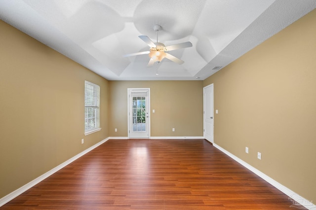 unfurnished room featuring visible vents, baseboards, a tray ceiling, wood finished floors, and a ceiling fan