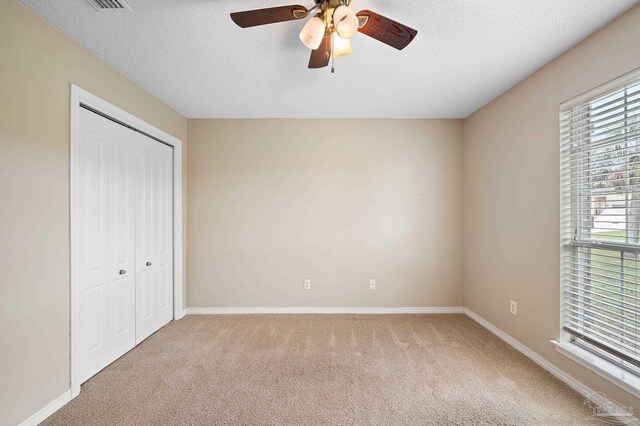 unfurnished bedroom with light carpet, a textured ceiling, ceiling fan, and a closet