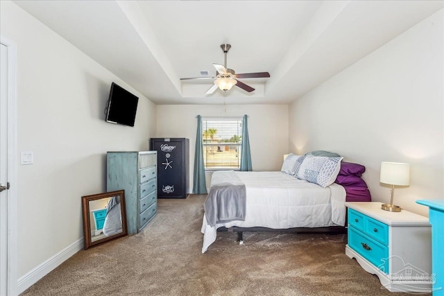 carpeted bedroom with a raised ceiling and ceiling fan