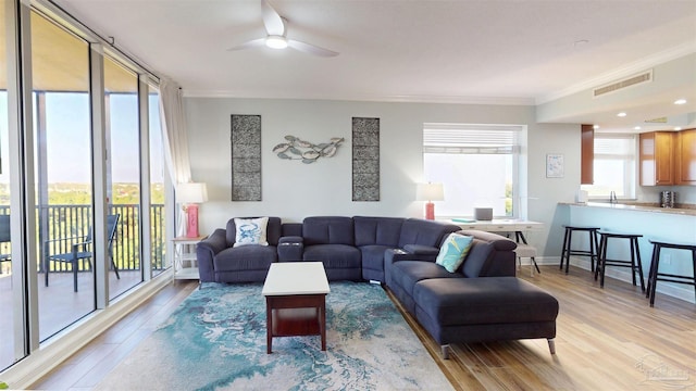 living area featuring ornamental molding, light wood-style flooring, and a ceiling fan
