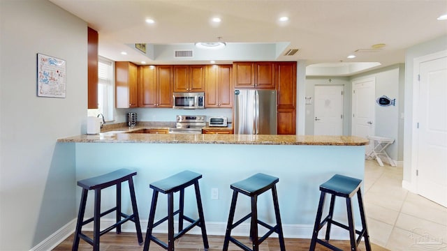 kitchen with appliances with stainless steel finishes, a peninsula, a sink, light stone counters, and a breakfast bar area