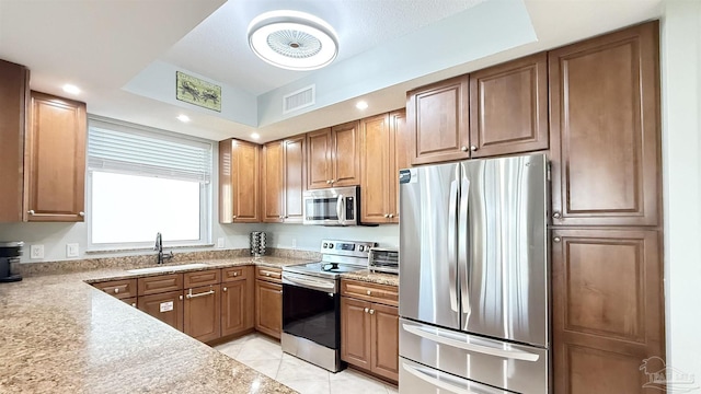 kitchen with stainless steel appliances, a sink, brown cabinetry, and light tile patterned floors