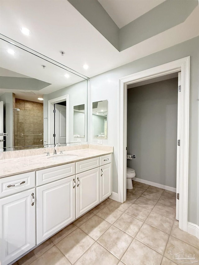 bathroom with toilet, tiled shower, tile patterned floors, vanity, and baseboards