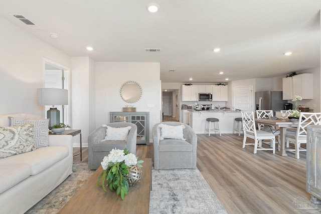 kitchen with white cabinets, appliances with stainless steel finishes, light hardwood / wood-style floors, and an island with sink