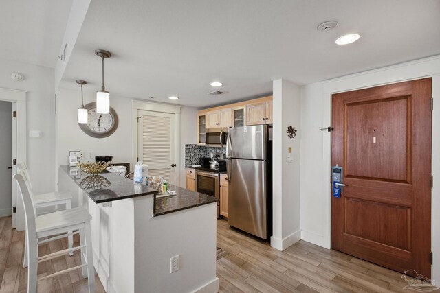 kitchen featuring pendant lighting, decorative backsplash, a kitchen bar, light hardwood / wood-style floors, and appliances with stainless steel finishes