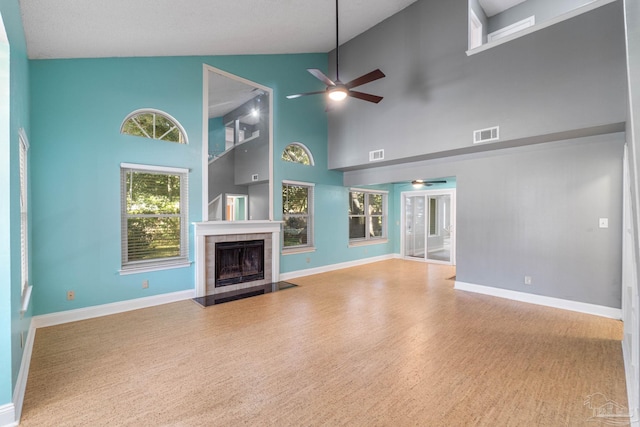 unfurnished living room featuring hardwood / wood-style floors, ceiling fan, a tile fireplace, and high vaulted ceiling