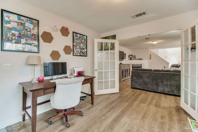 office space featuring a textured ceiling, light wood-style flooring, visible vents, french doors, and a tiled fireplace