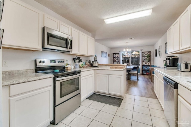 kitchen with a peninsula, white cabinets, hanging light fixtures, appliances with stainless steel finishes, and an inviting chandelier