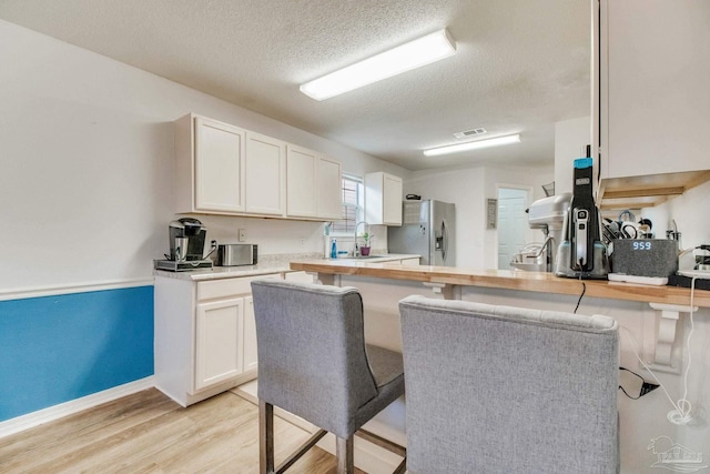 kitchen featuring stainless steel fridge with ice dispenser, butcher block counters, a breakfast bar, light wood-style floors, and white cabinetry