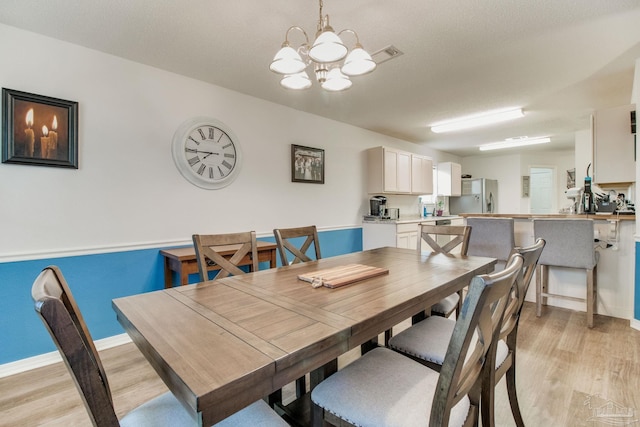 dining area with light wood-type flooring, a textured ceiling, baseboards, and an inviting chandelier