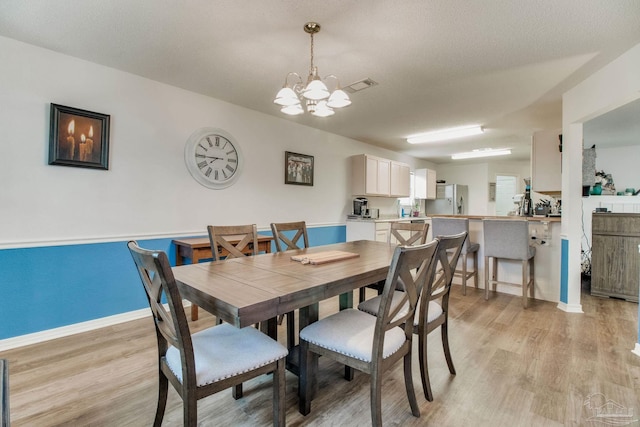 dining space featuring a notable chandelier, visible vents, light wood-style floors, a textured ceiling, and baseboards