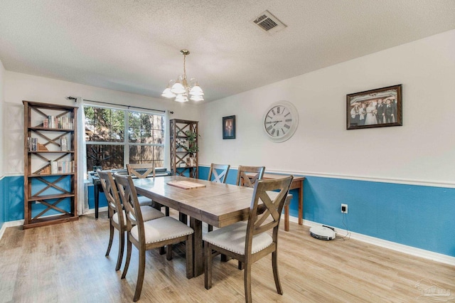 dining space featuring a textured ceiling, a notable chandelier, visible vents, baseboards, and light wood finished floors