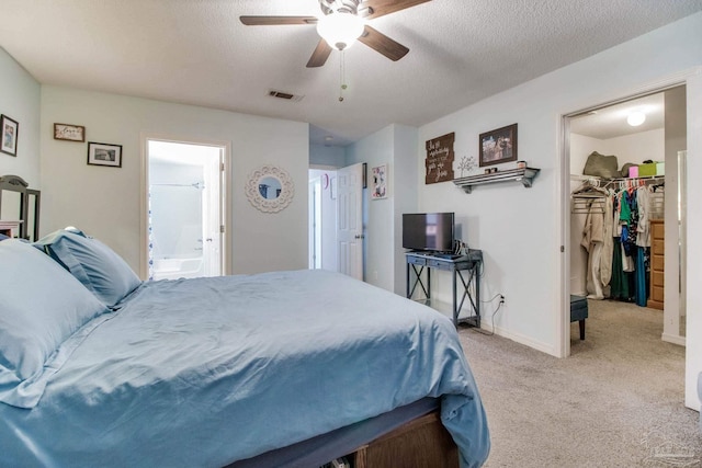 bedroom with a spacious closet, visible vents, a textured ceiling, and light colored carpet