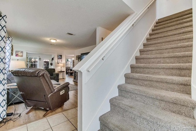 stairs featuring tile patterned flooring, visible vents, and a textured ceiling