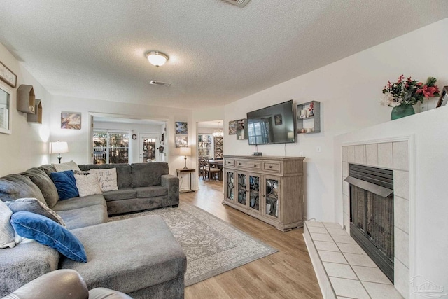 living area with light wood finished floors, visible vents, a textured ceiling, and a tile fireplace