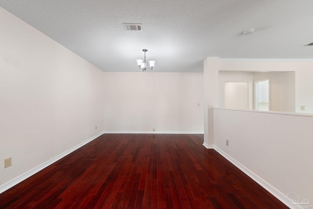 spare room with an inviting chandelier, a textured ceiling, and dark hardwood / wood-style flooring