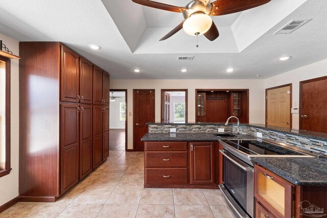 kitchen with decorative backsplash, a raised ceiling, a textured ceiling, ceiling fan, and stainless steel electric range oven