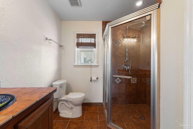 bathroom featuring vanity, tile patterned flooring, a textured ceiling, toilet, and a shower with door