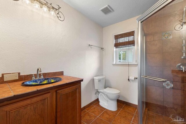 bathroom featuring tile patterned floors, a shower with door, vanity, and toilet