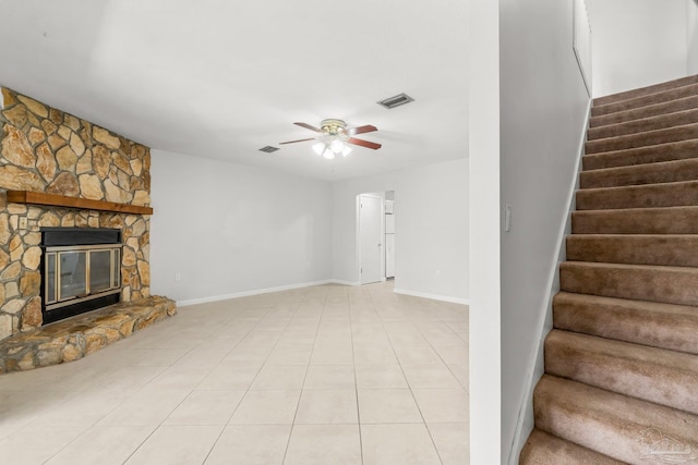 unfurnished living room with light tile patterned floors, visible vents, ceiling fan, a stone fireplace, and stairs