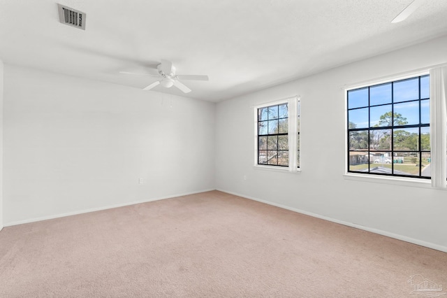 carpeted spare room with plenty of natural light, visible vents, ceiling fan, and baseboards