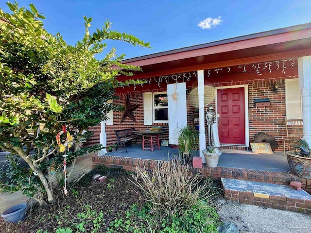 doorway to property with a porch and brick siding