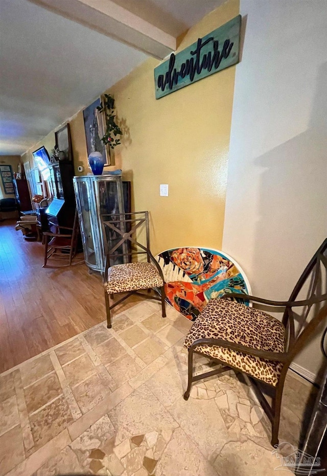 living area featuring stone tile floors, baseboards, and beamed ceiling