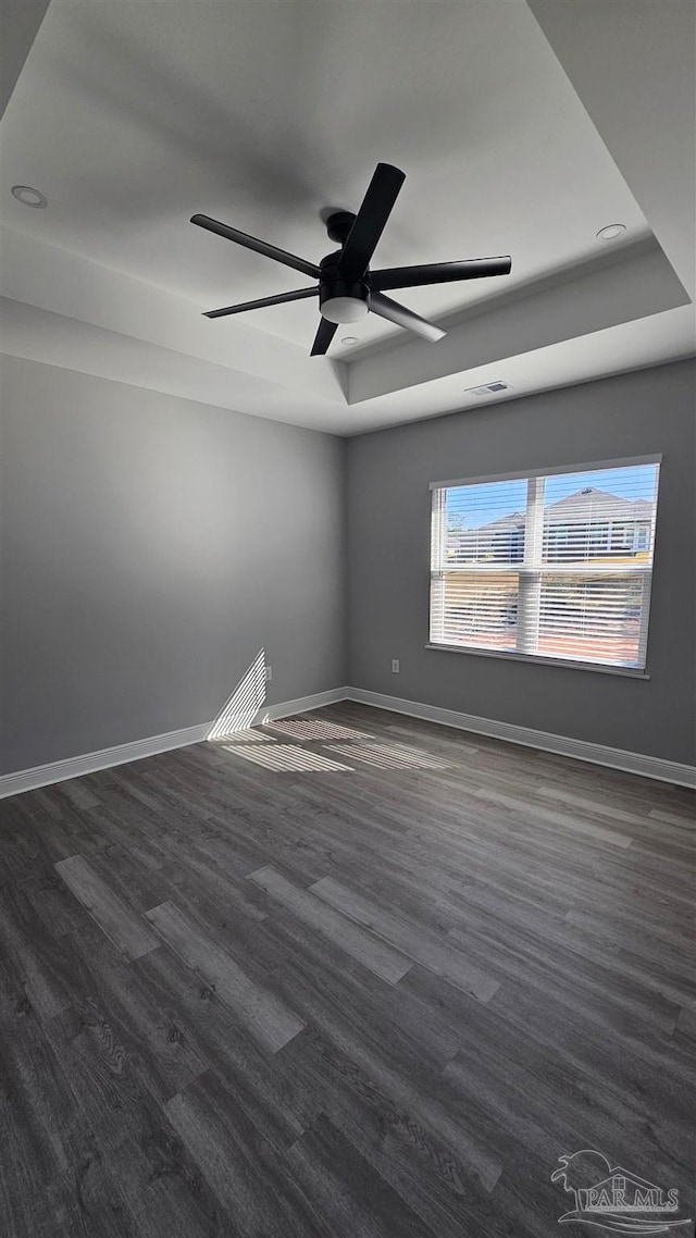 empty room featuring ceiling fan, a tray ceiling, and dark hardwood / wood-style flooring