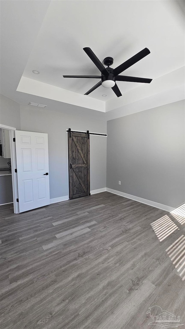 unfurnished bedroom featuring ceiling fan, a tray ceiling, dark hardwood / wood-style flooring, and a barn door