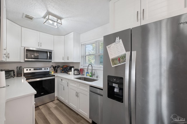 kitchen featuring a textured ceiling, appliances with stainless steel finishes, white cabinetry, sink, and light wood-type flooring