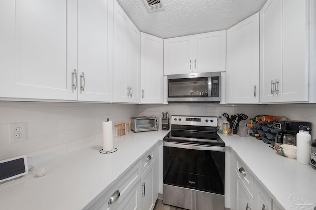 kitchen featuring a textured ceiling, stainless steel appliances, backsplash, and white cabinetry