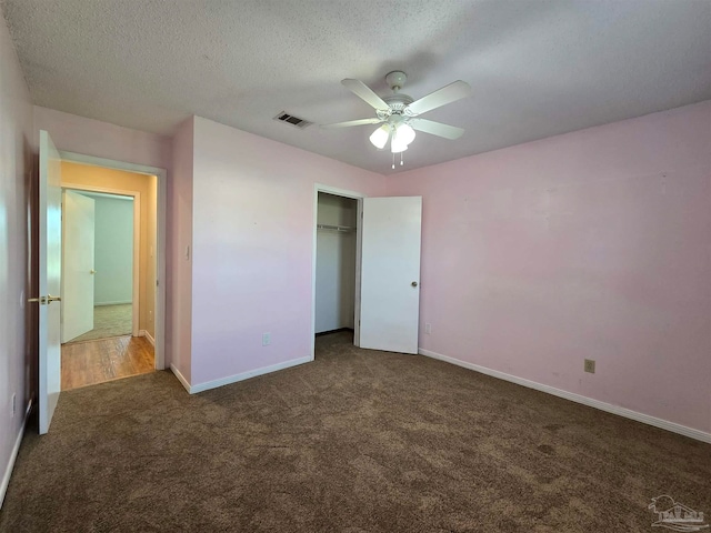 unfurnished bedroom featuring dark colored carpet, a textured ceiling, a closet, and ceiling fan