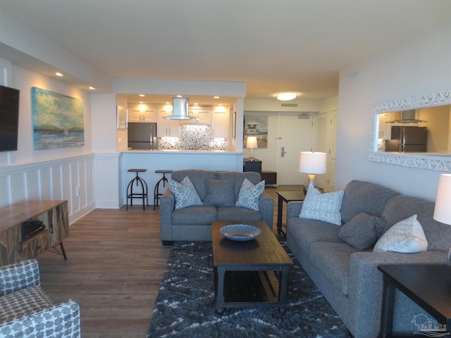 living room with visible vents, a decorative wall, dark wood-style flooring, and wainscoting