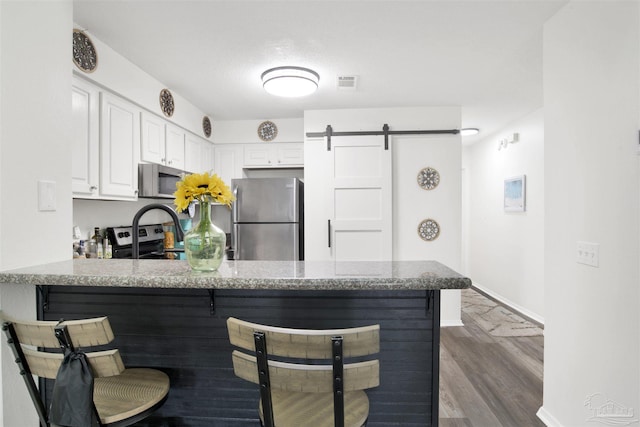 kitchen with appliances with stainless steel finishes, light stone countertops, white cabinets, a barn door, and kitchen peninsula